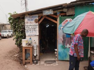 Auguy standing proudly in front of his atelier, surrounded by his sculptures and artworks, showcasing his dedication to preserving Congo's cultural heritage.